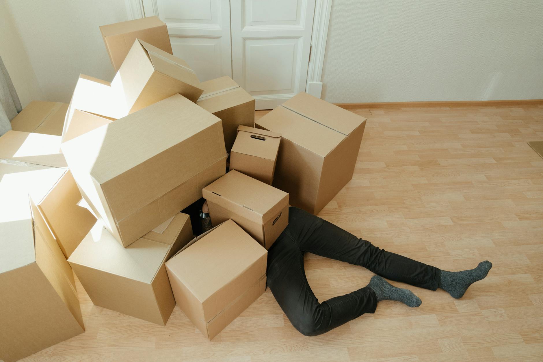 Person lying on the floor under a huge pile of boxes