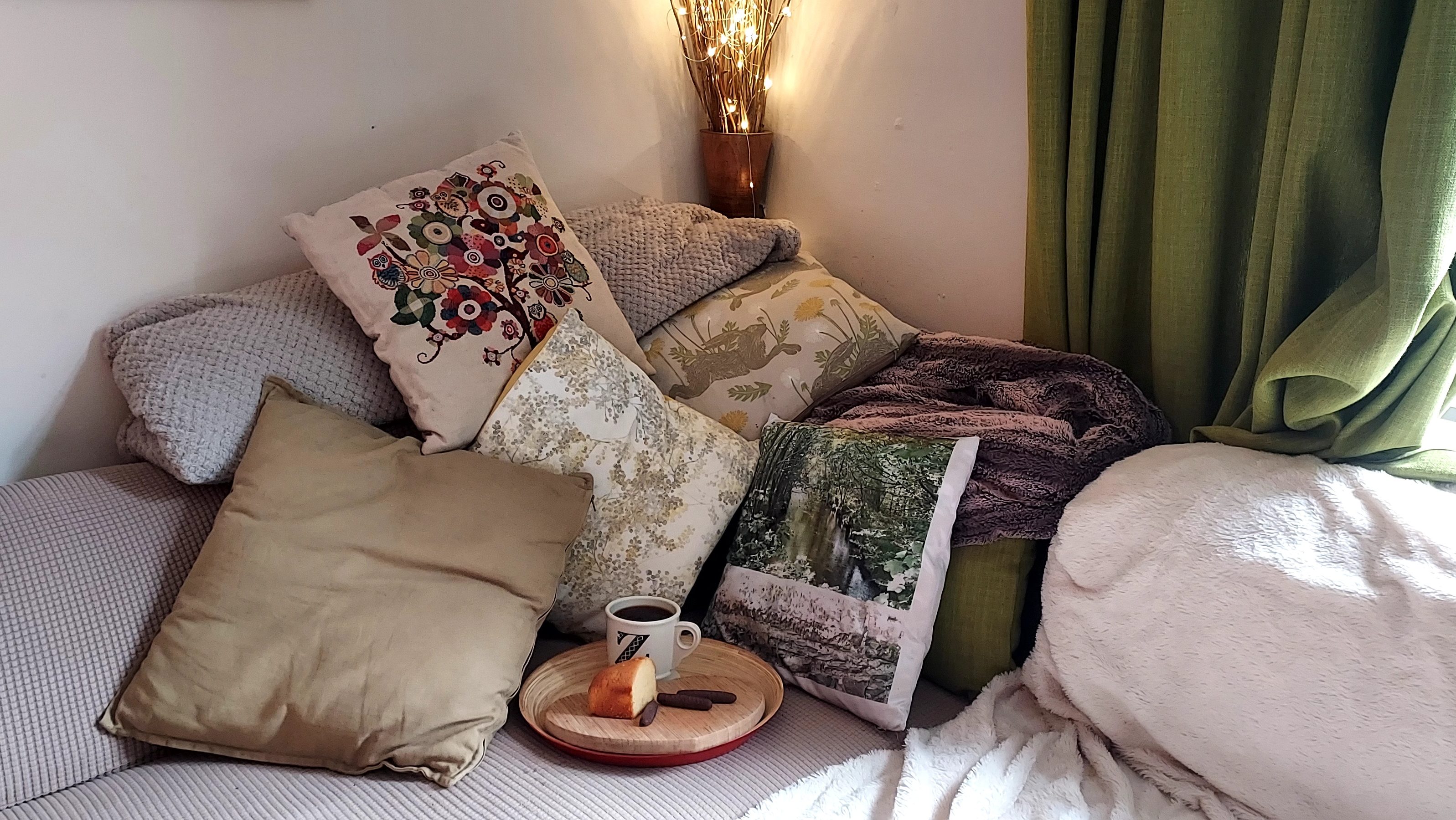 Sunlight coming into room with cosy light, comfy blankets and cushions, coffee and cake Sunlight coming into room with cosy light, comfy blankets and cushions, coffee and cake