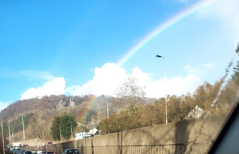 Rainbow falling onto a road with hillside beyond