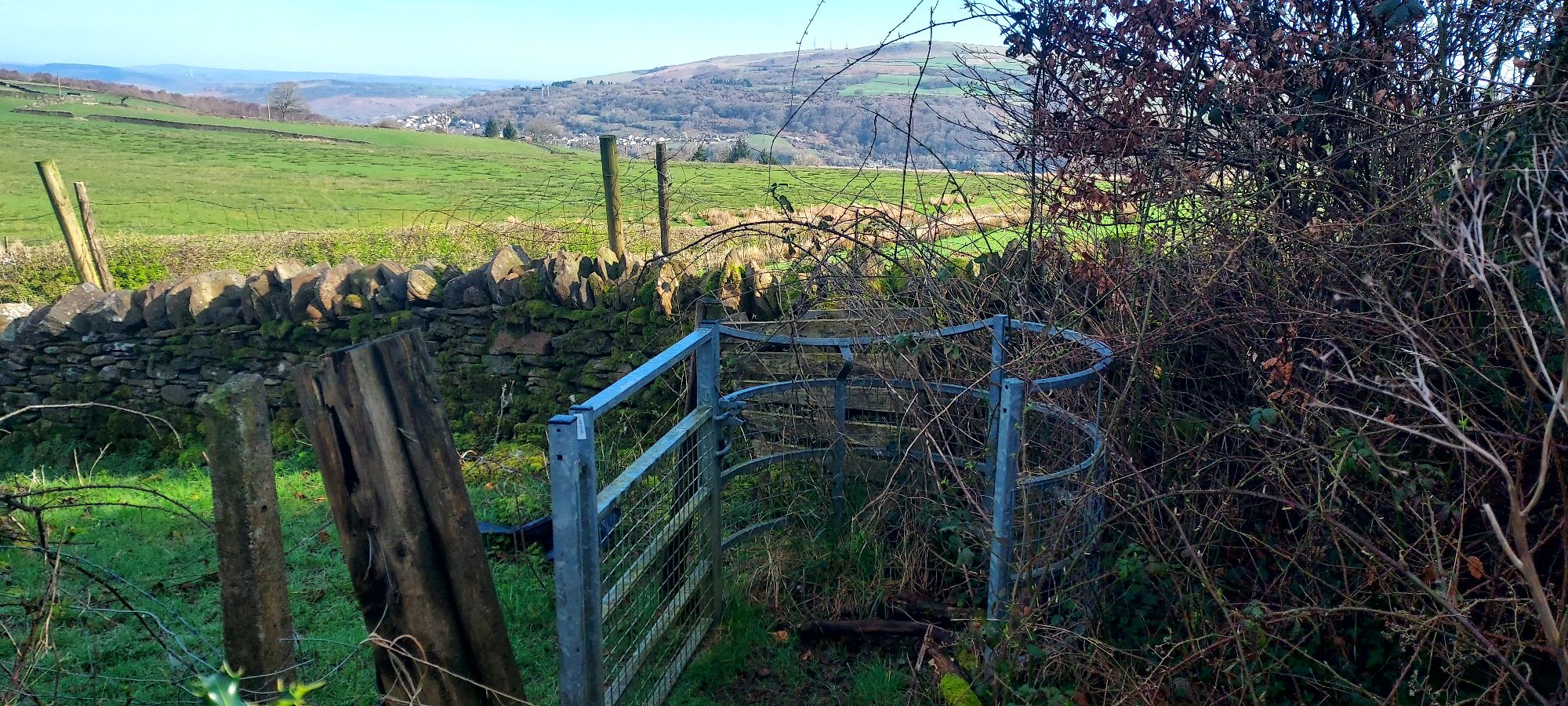 Kissing gate onto field top path with mountain views beyond